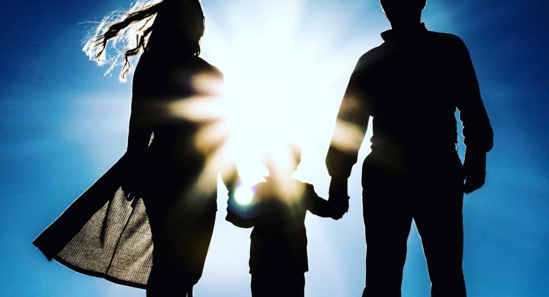 Parents holding hands of child with sun in the background