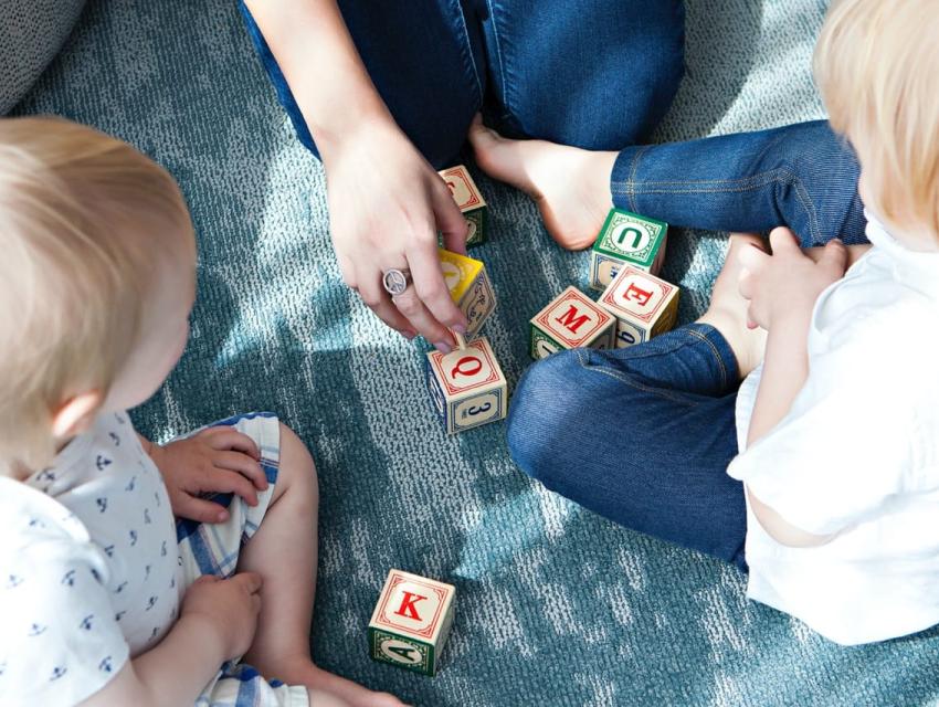 Parent playing with 2 young children and alphabet blocks