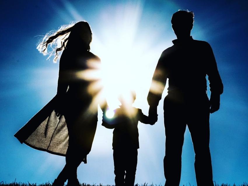 Parents holding hands of child with sun in the background